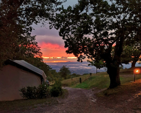 Atardecer en Camping Lucherino, Toscana, Italia, con una tienda, árboles y paisaje panorámico.