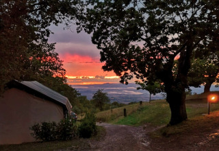 Atardecer en Camping Lucherino, Toscana, Italia, con una tienda, árboles y paisaje panorámico.