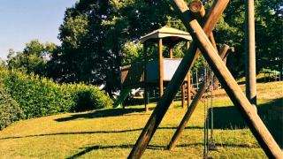 Playground at Camping Lucherino in Tuscany, Italy, featuring swings and a wooden playhouse on a hill.
