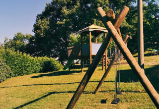 Spielplatz im Camping Lucherino, Toskana, Italien, mit Schaukeln und Holzhäuschen auf grünem Hügel.