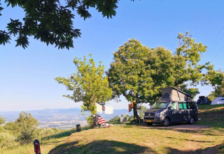Camping Lucherino in Toscana, Italia, con camper, alberi e splendida vista sulle colline e sulla valle.