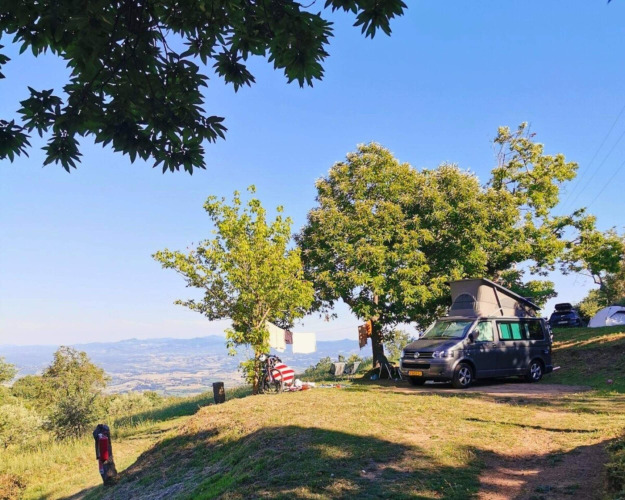Camping Lucherino in der Toskana, Italien, mit Wohnmobil, Bäumen und Aussicht auf Hügel und Tal.