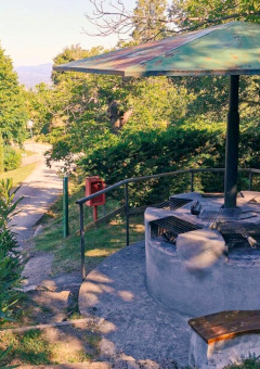 Outdoor barbecue area with benches at Camping Lucherino in Tuscany, Italy, shaded by trees and a canopy.