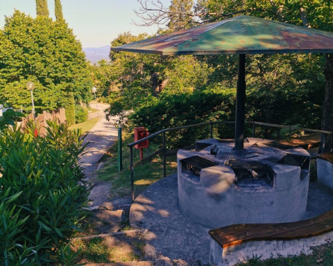 Área de barbacoa al aire libre en Camping Lucherino, Toscana, Italia, rodeada de bancas y vegetación.
