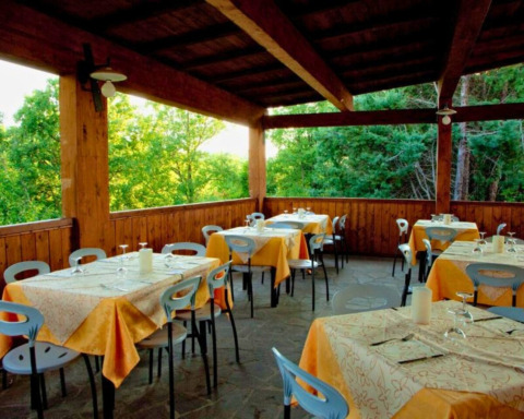 Zona de comedor exterior cubierta con mesas puestas en Camping Lucherino, en la Toscana, Italia, junto al bosque.