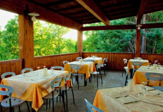 Terrasse couverte avec tables dressées au Camping Lucherino, en Toscane, Italie, entourée de verdure.