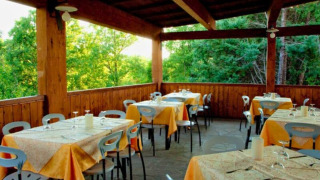 Zona de comedor exterior cubierta con mesas puestas en Camping Lucherino, en la Toscana, Italia, junto al bosque.