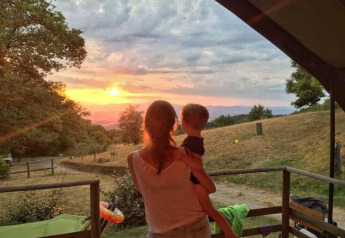 En kvinde holder et barn og nyder solnedgangen fra Safari Tent Valley på Camping Lucherino i Italien.