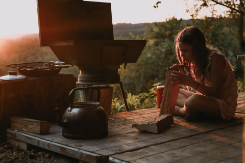 Mädchen spaltet Holz neben einem Außengrill bei Sonnenuntergang im Feather Down Rochefort-Ardenne, Belgien.
