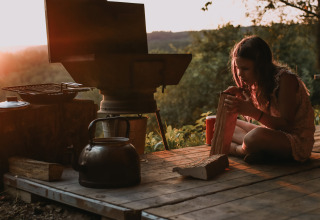 Ragazza che spacca legna vicino a una cucina all'aperto al tramonto a Feather Down Rochefort-Ardenne, Belgio.