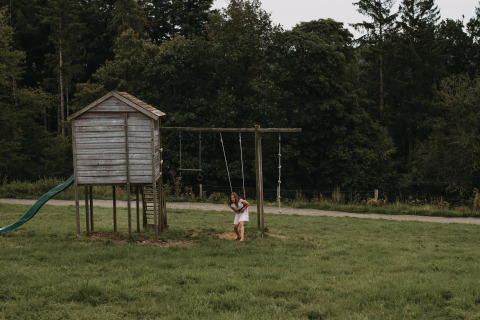 Une fille joue sur une balançoire près d’une cabane en bois dans un pré près de Nassogne, Luxembourg, Belgique.