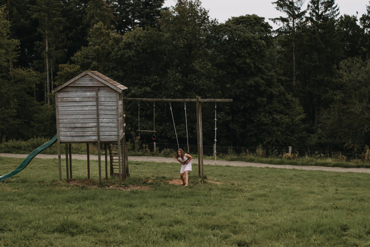 Een meisje speelt op een schommel bij een houten speelhuisje in het groen vlakbij Nassogne, Luxemburg, België.