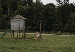 Ein Mädchen spielt an einer Schaukel neben einem Holzhaus im Grünen bei Nassogne, Luxemburg, Belgien.