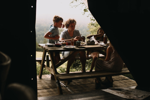 Gezin eet buiten aan een houten tafel bij Feather Down Rochefort-Ardenne, België, met uitzicht op de natuur.