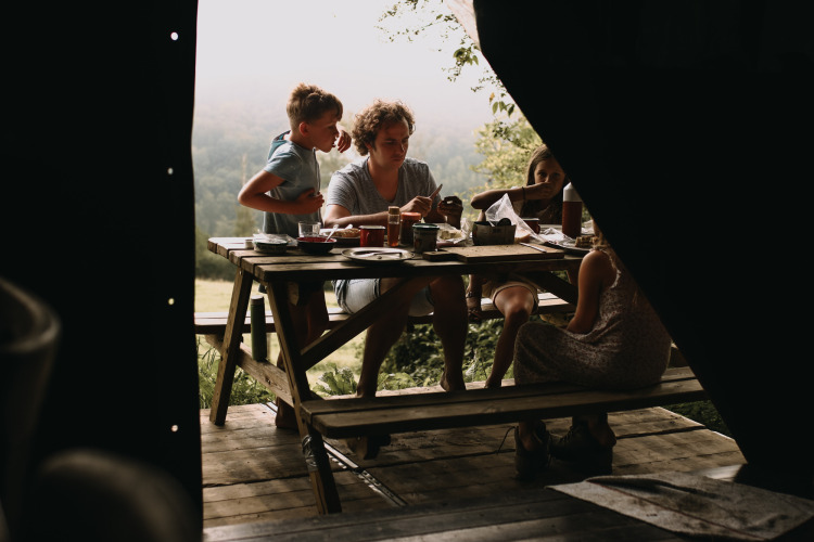 Family enjoys an outdoor meal at a wooden table with scenic views at Feather Down Rochefort-Ardenne, Belgium.