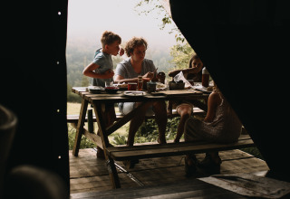Gezin eet buiten aan een houten tafel bij Feather Down Rochefort-Ardenne, België, met uitzicht op de natuur.