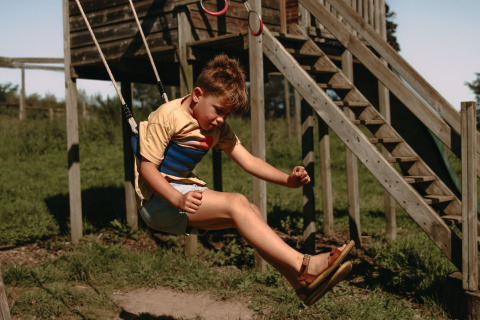 Junge schaukelt fröhlich auf dem Spielplatz im Feather Down Rochefort-Ardenne Ferienpark in Belgien.