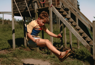 Junge schaukelt fröhlich auf dem Spielplatz im Feather Down Rochefort-Ardenne Ferienpark in Belgien.