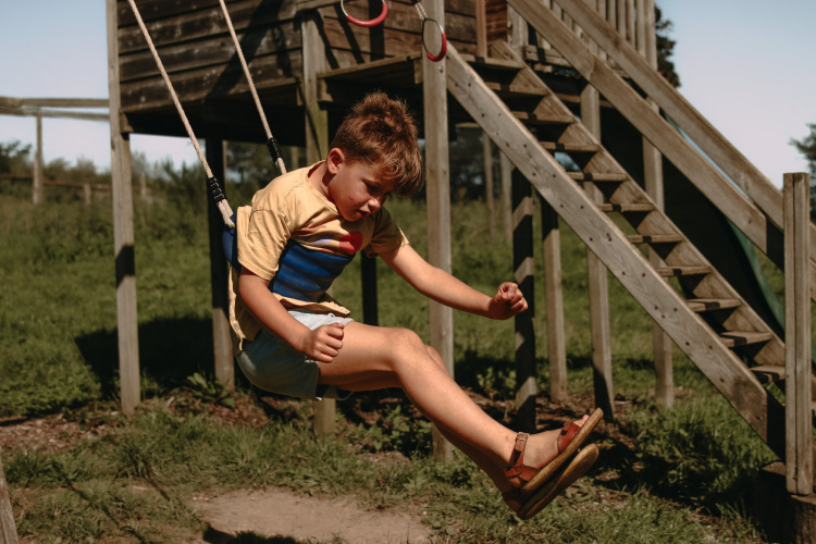 Jongen speelt op de schommel op de speeltuin van Feather Down Rochefort-Ardenne vakantiepark in België.