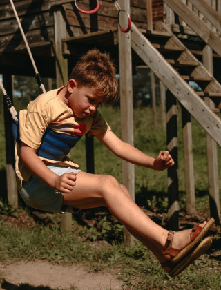 Dreng nyder at gynge udendørs på legepladsen ved Feather Down Rochefort-Ardenne feriepark i Belgien.