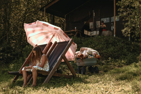 A girl relaxes on a deckchair under a parasol at Feather Down Rochefort-Ardenne in Belgium Luxembourg.