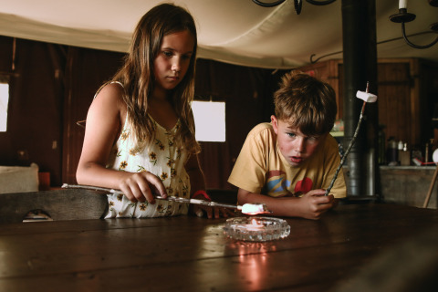 Twee kinderen roosteren marshmallows boven een kaars in huis bij Feather Down Rochefort-Ardenne.