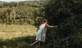 Niña con vestido de verano recoge bayas cerca de Nassogne, Bélgica, rodeada de prados y bosques verdes.