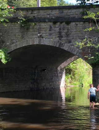 Un hombre y un niño caminan por aguas bajas bajo un puente de piedra cerca de Nassogne, Bélgica.