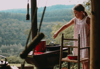 Een meisje kookt buiten op een barbecue met zicht op beboste heuvels in Rochefort-Ardenne, België.