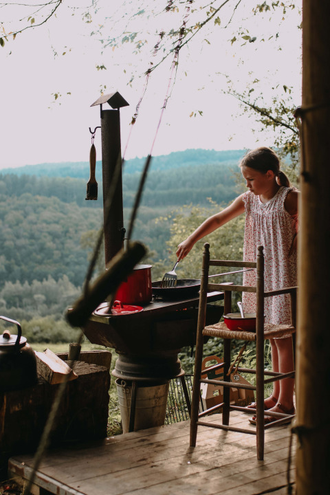 Une fille cuisine dehors sur un gril avec vue sur des collines boisées à Rochefort-Ardenne, Belgique.