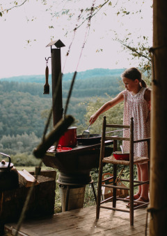 Una niña cocina al aire libre en una parrilla con vistas de colinas boscosas en Rochefort-Ardenne, Bélgica.