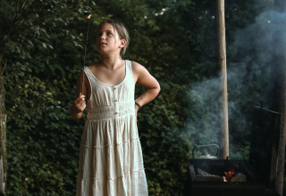 Meisje in witte jurk roostert marshmallows op kampvuur bij Feather Down Rochefort-Ardenne in België.