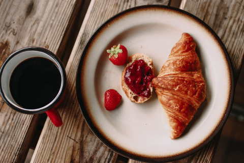 Een bord met croissant, aardbeien, brood met jam en een kop koffie bij Feather Down Rochefort-Ardenne.