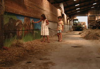 Zwei Kinder spielen im Heuschuppen im Feather Down Rochefort-Ardenne, Belgien, mit Traktor im Hintergrund.