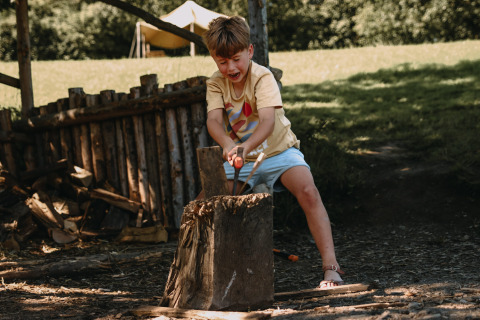 Een kind hakt hout buiten bij Feather Down Rochefort-Ardenne, een vakantiepark in België Luxemburg.