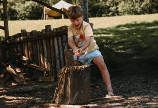 Een kind hakt hout buiten bij Feather Down Rochefort-Ardenne, een vakantiepark in België Luxemburg.