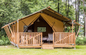 Safaritent met houten veranda en stoelen midden in het bos, slaapkamer en bed zichtbaar binnen.
