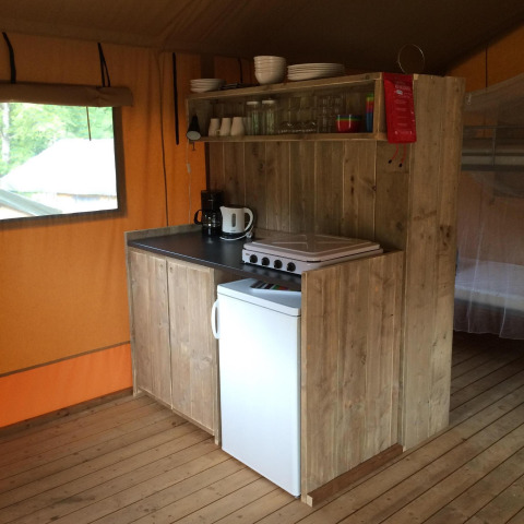 Pequeña cocina en tienda safari con armarios de madera, placa eléctrica, mini nevera y cafetera.