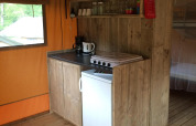 Kleine keuken in safaritent met houten kastjes, kookplaat, mini-koelkast en koffiezetapparaat.