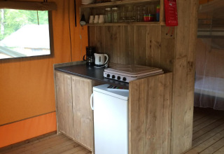 Pequeña cocina en tienda safari con armarios de madera, placa eléctrica, mini nevera y cafetera.