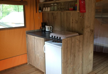 Pequeña cocina en tienda safari con armarios de madera, placa eléctrica, mini nevera y cafetera.
