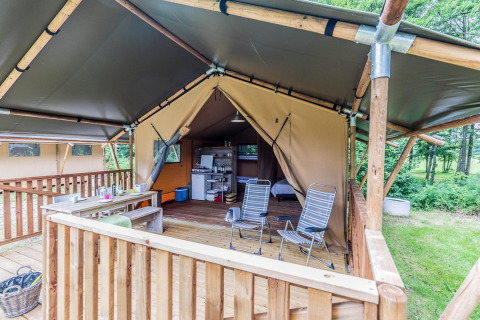 Tienda safari con terraza de madera, mesa de comedor, sillas y área de cocina en un entorno natural.
