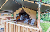Udendørs safari telt med træterrasse, spisebord, stole og køkkenområde i naturskøn omgivelser.