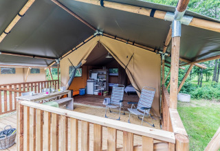 Tienda safari con terraza de madera, mesa de comedor, sillas y área de cocina en un entorno natural.