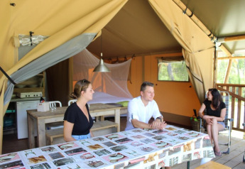 Tre persone si rilassano all'interno di una tenda safari con arredi in legno e luce naturale esterna.