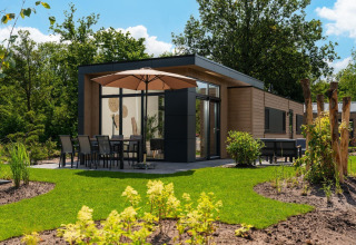 Lodge Cannenburch moderno con sombrilla, comedor y jardín en Veluwepark de Bosgraaf, Países Bajos.