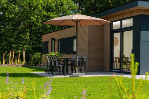 Terrasse der Cannenburch-Lodge im Veluwepark de Bosgraaf, Niederlande, mit Tisch, Stühlen und Sonnenschirm.