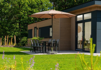 Terrasse der Cannenburch-Lodge im Veluwepark de Bosgraaf, Niederlande, mit Tisch, Stühlen und Sonnenschirm.