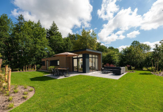 Lodge moderno con terraza y muebles de exterior, rodeado de vegetación en Veluwepark de Bosgraaf, Países Bajos.