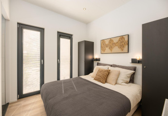 Moderne slaapkamer met tweepersoonsbed, zwarte kasten en grote ramen in Cannenburch, Veluwepark de Bosgraaf.